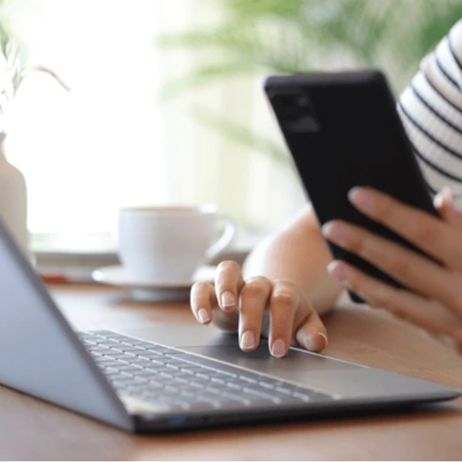 Unknown person using the laptop while holding their phone in their other hand